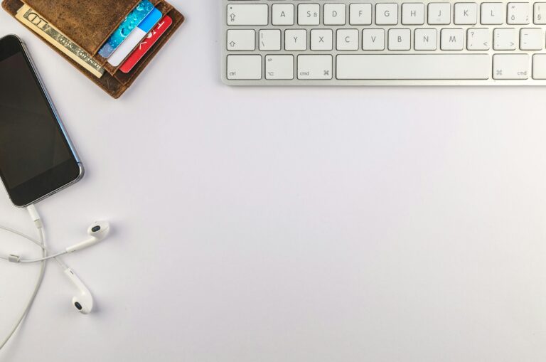 Flat lay of minimalist desk setup featuring a smartphone, keyboard, earphones, and wallet for productivity inspiration.